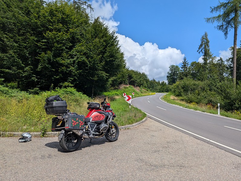 Petualangan BMW R1250GS merah saya di sisi jalan di Jerman. Jalan itu berliku ke kejauhan melalui pepohonan.